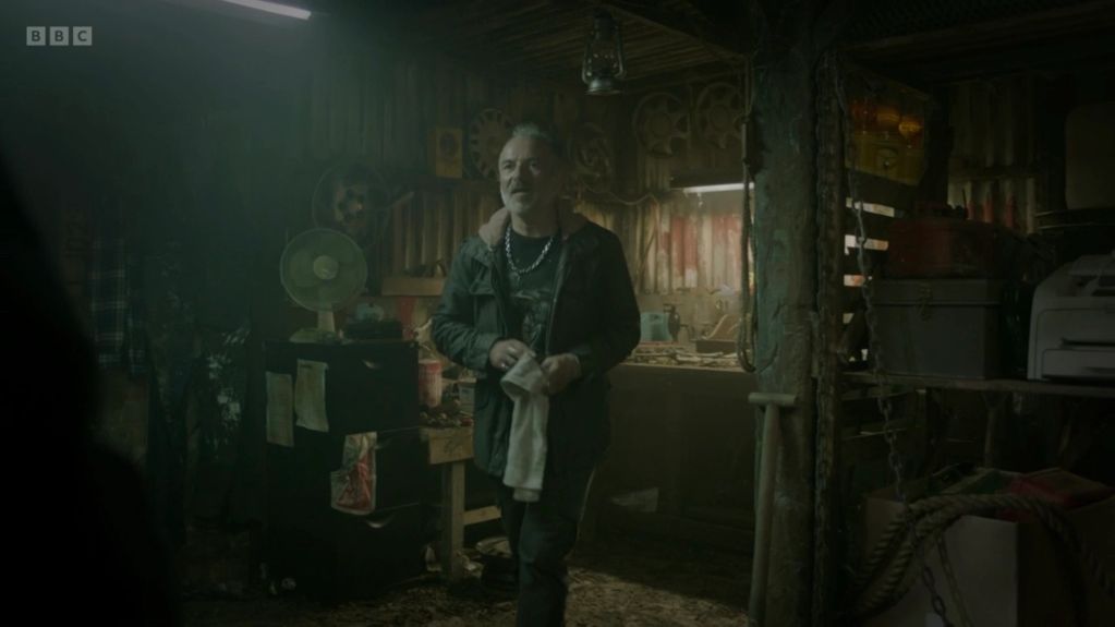 Man standing in a dimly lit, cluttered workshop.