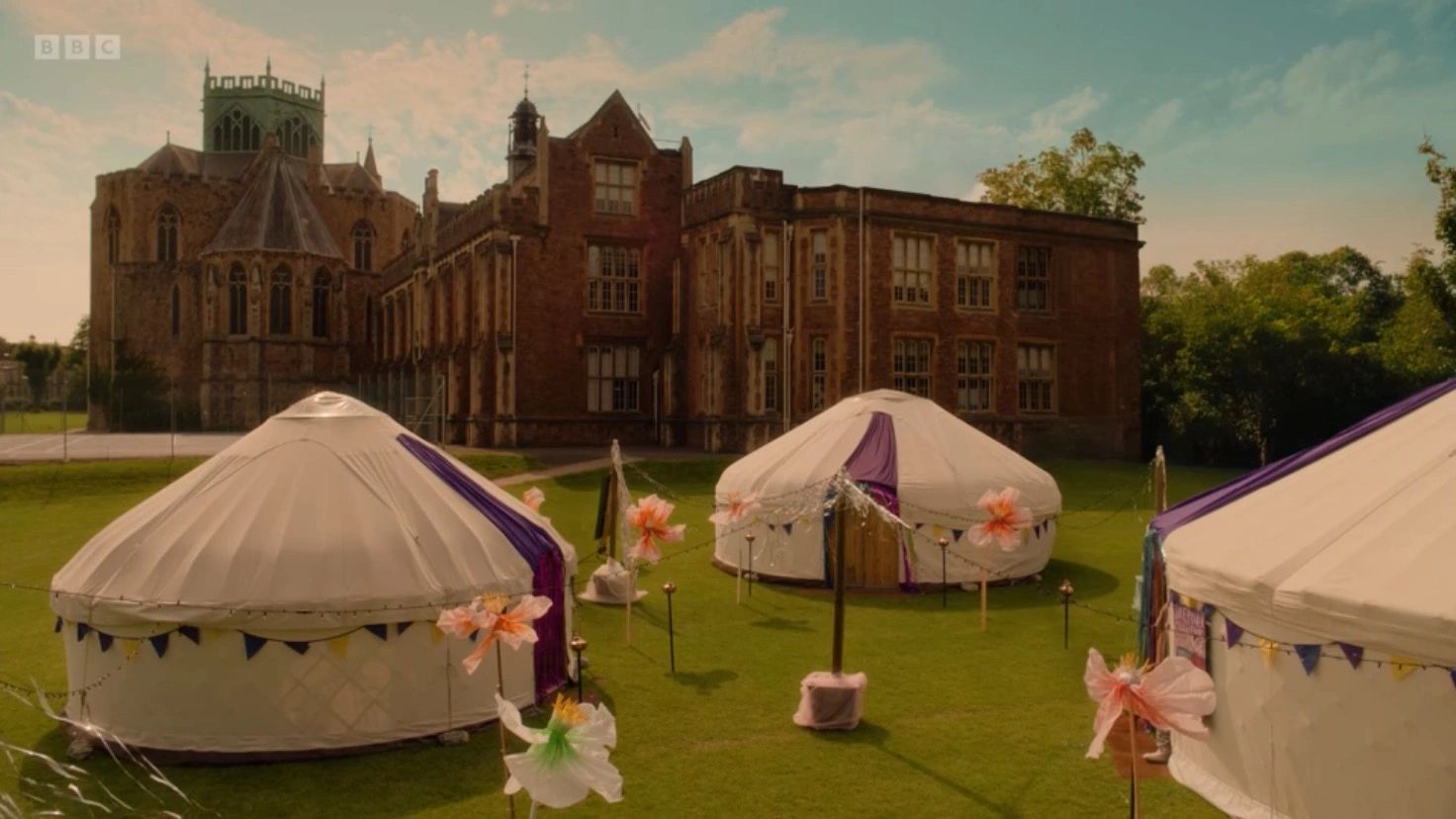 Yurt tents set up on green lawn near historic building.