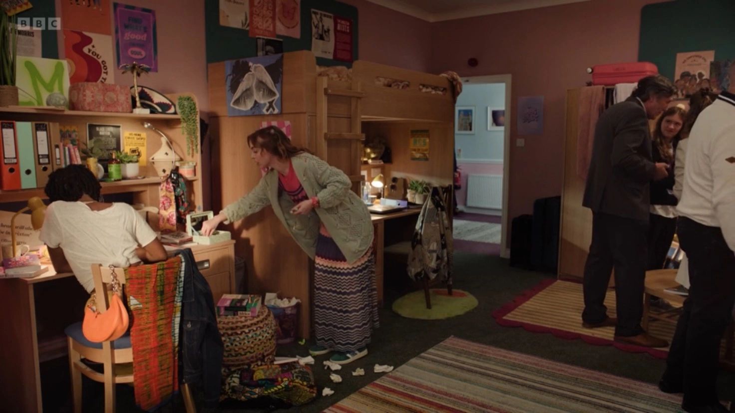 Students in a dorm room with bunk beds and cluttered desks.