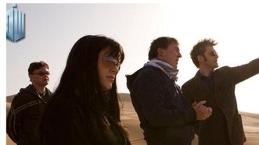 Four people stand in a desert, one pointing.