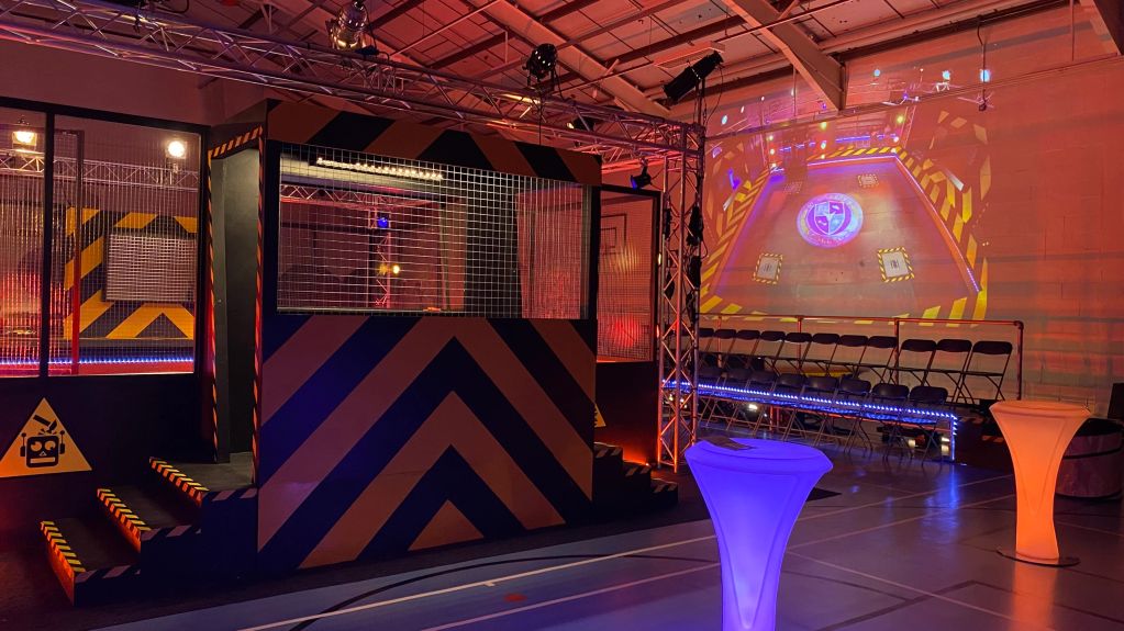 Indoor gaming arena with neon lights and projection screen.