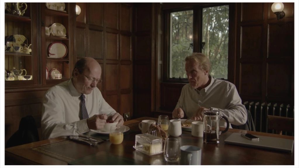 Two men having breakfast in a wooden-paneled room.