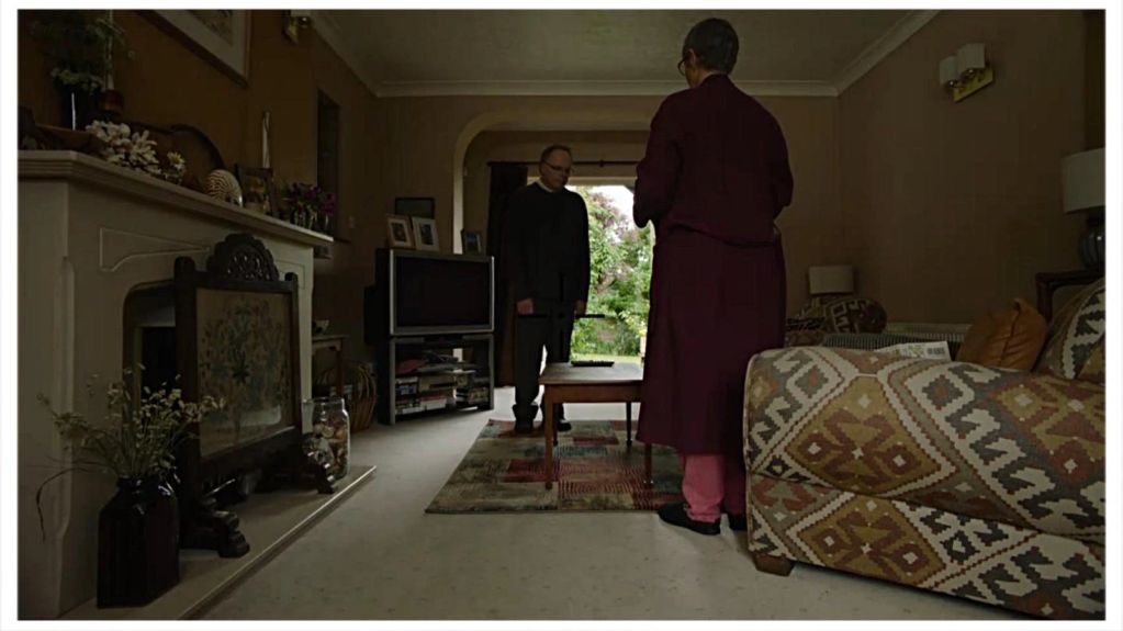 Two men talking in a dimly lit living room.
