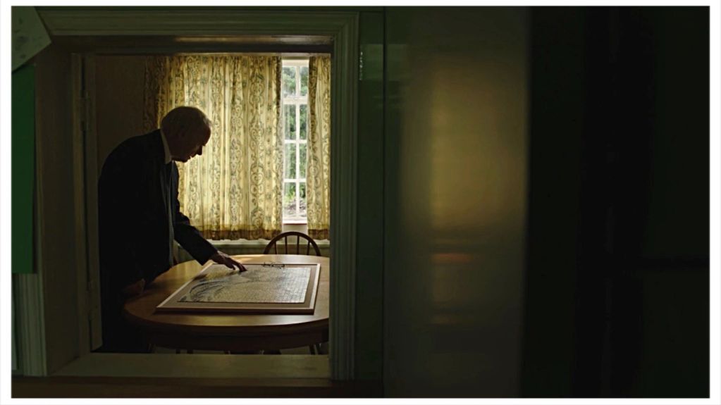 Man examining artwork on a table by a window.