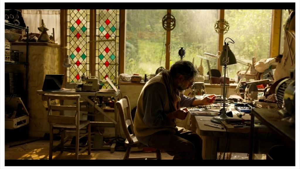 Man working intently at a cluttered workbench in a warmly lit workshop.