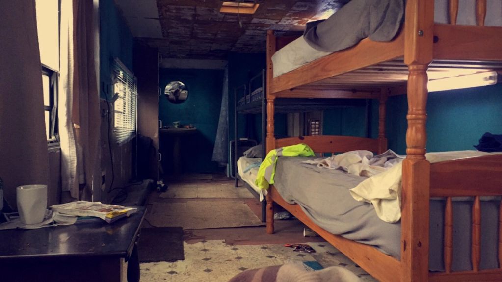 Wooden bunk beds in a dimly lit, cluttered room with teal walls.