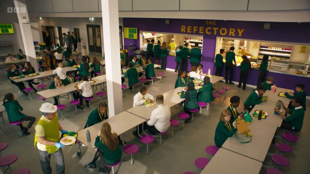 Students in a school cafeteria wearing green uniforms.