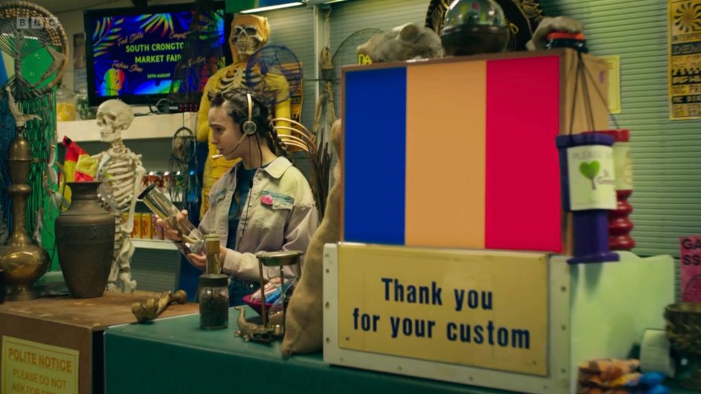 Woman in a market with skeleton displays and colorful signs.
