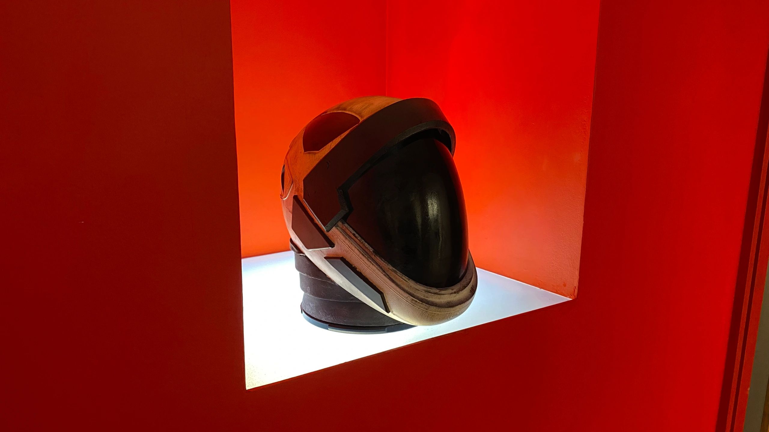 A futuristic helmet on display with red background.