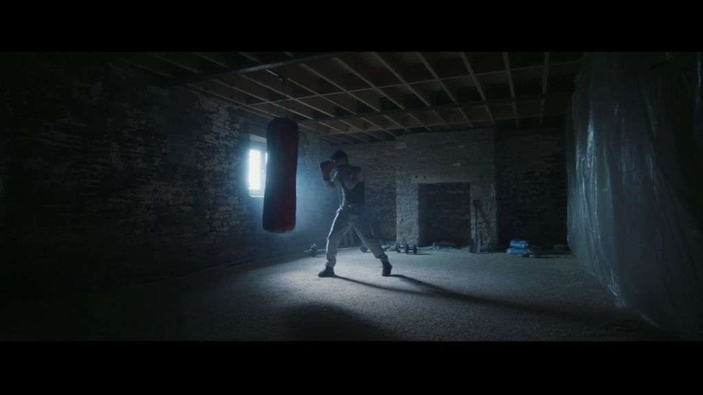 Boxer training in a dimly lit underground room with a punching bag.