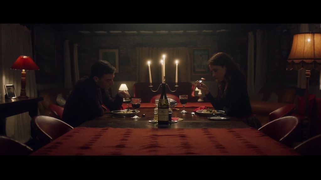 Two people eating dinner by candlelight at a long table.
