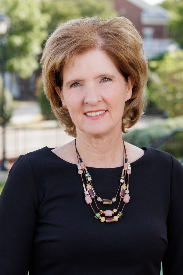 Smiling woman with short brown hair wearing a black top and colorful beaded necklace.