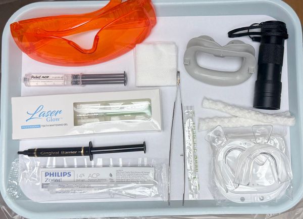 Tray with various dental whitening tools including gel, syringes, and protective glasses.