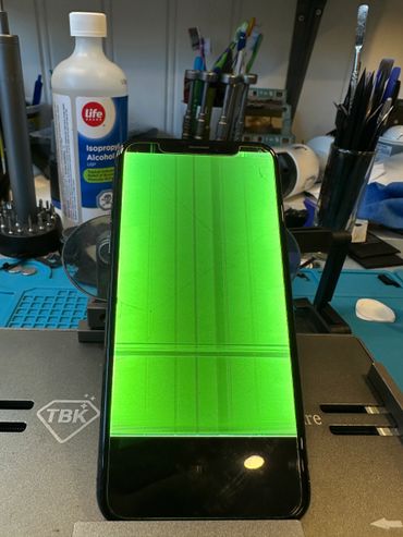 Smartphone with a green distorted screen on a repair desk.