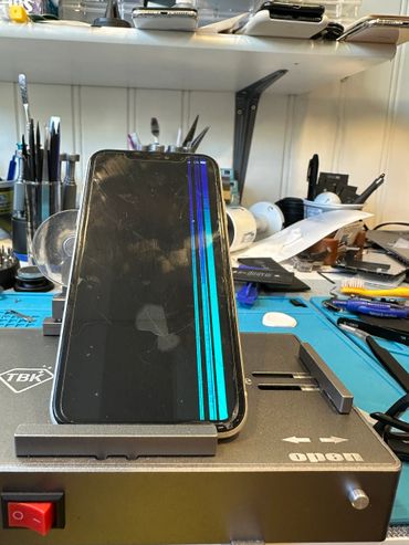A cracked smartphone screen with vertical blue lines on a repair station.