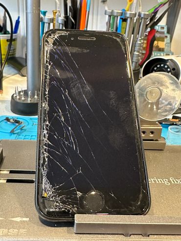 A smartphone with a severely cracked screen on a workbench.