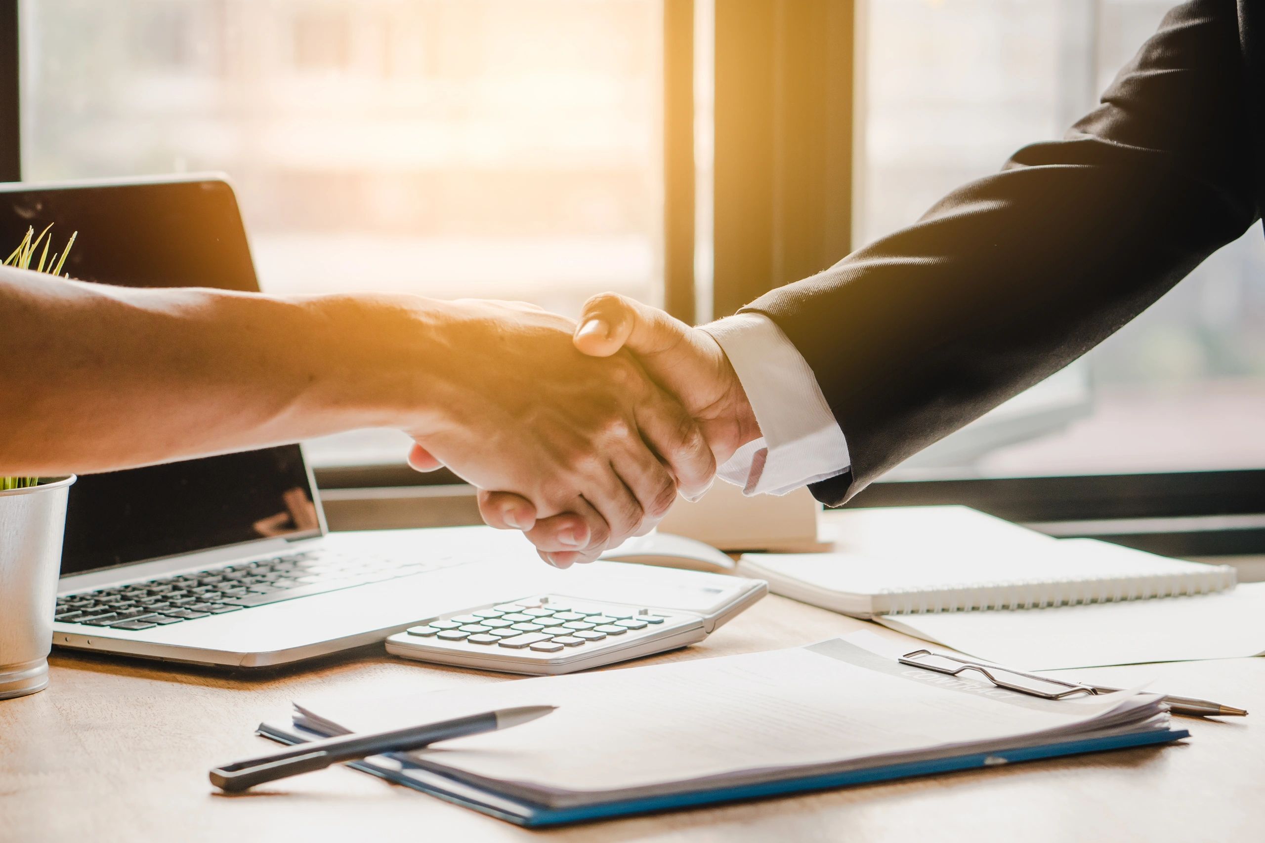 Business people shaking hands over a desk with a laptop. 