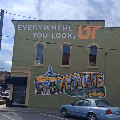 A large "Greetings from Fayetteville" colorful mural on a green brick building in Tennessee.