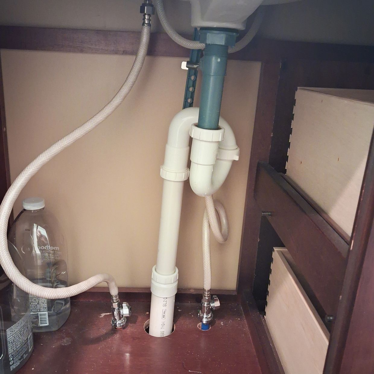 Licensed inspector checking P-trap and supply lines under a bathroom vanity.