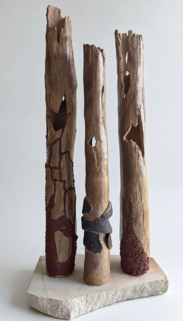 Sculpture of three tall, textured wooden pillars on a stone base.
