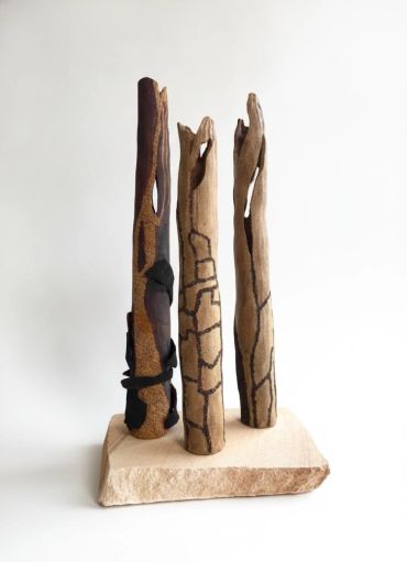 Three decorated wooden sticks on a stone base.
