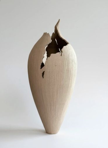 A tall, beige ceramic vase with a large crack and missing section.