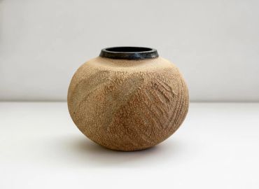 Textured round ceramic vase with black rim.