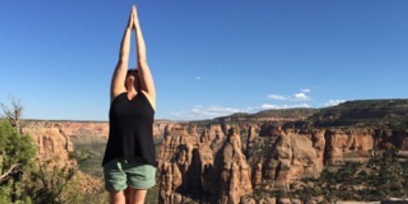 Person practicing yoga with arms raised against a canyon backdrop.
