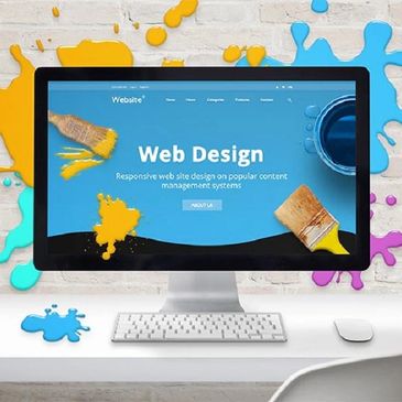 Modern workspace with a computer displaying web design and colorful paint splashes.