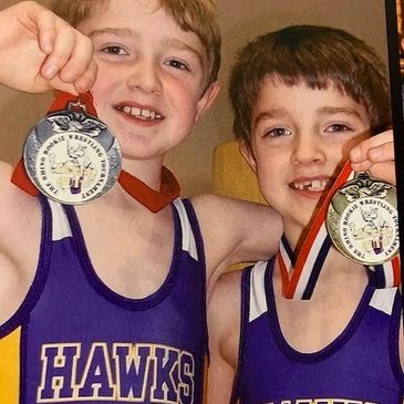 Two youth wrestlers, brothers, displaying their hard-earned wrestling medals