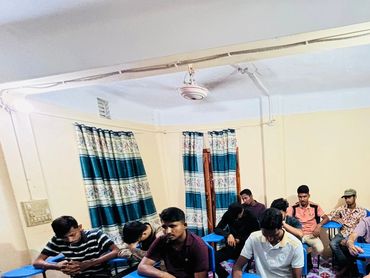 A group of men sitting indoors, some looking at their phones.