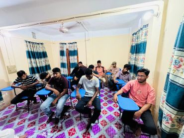 A group of men sitting indoors, some looking at their phones.