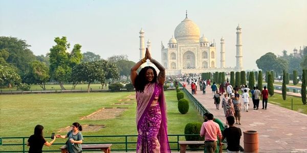 Woman in purple saree posing happily at the Taj Mahal.