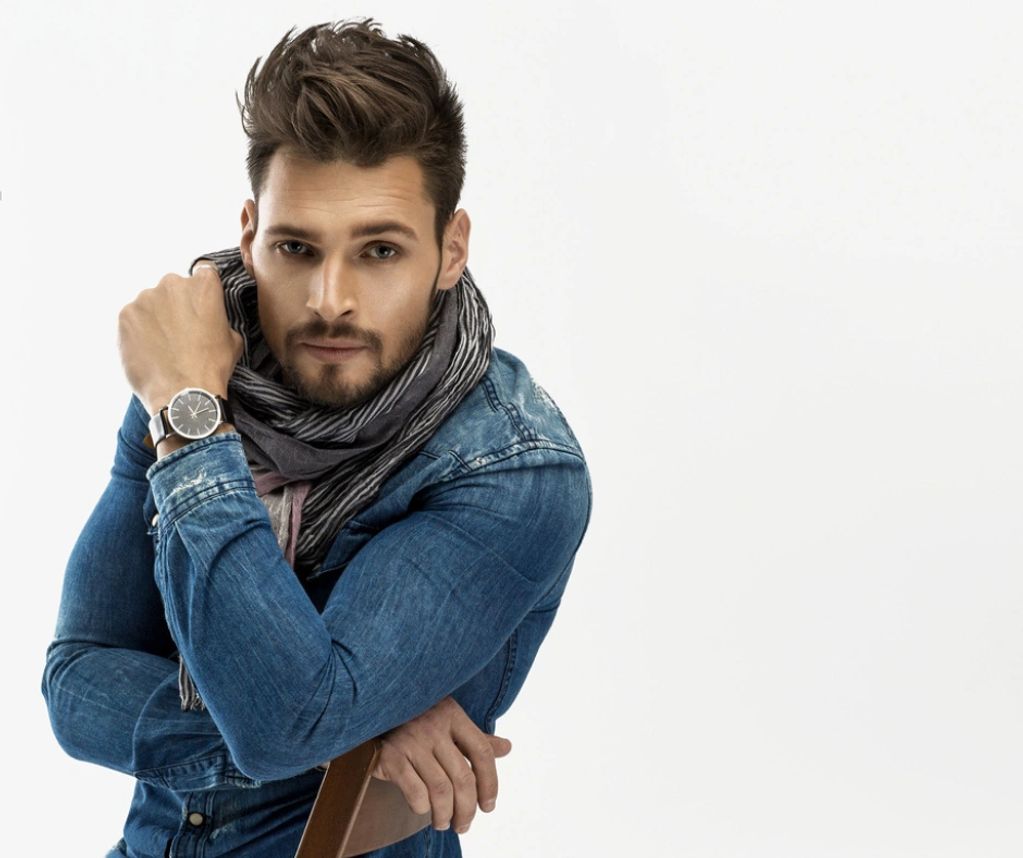 brunette male in his 20's wearing denim jacket and cotton scarf sitting on chair  