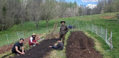 Four people gardening together in a fenced outdoor area on a sunny day.
