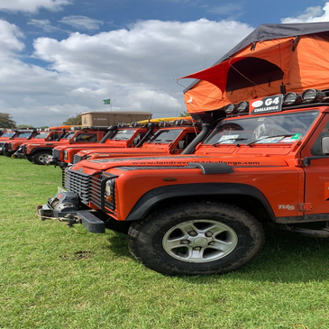 Row of orange Land Rover vehicles on grass under a partly cloudy sky.