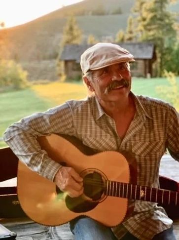Smiling man playing guitar outdoors during sunset.