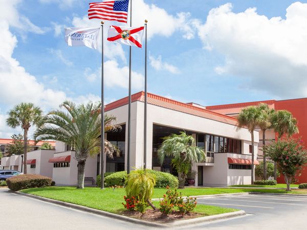 A hotel exterior with flags, palm trees, and a parking lot.