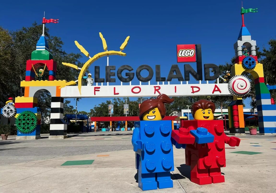 Two Lego figures stand in front of the Legoland Florida entrance gate.