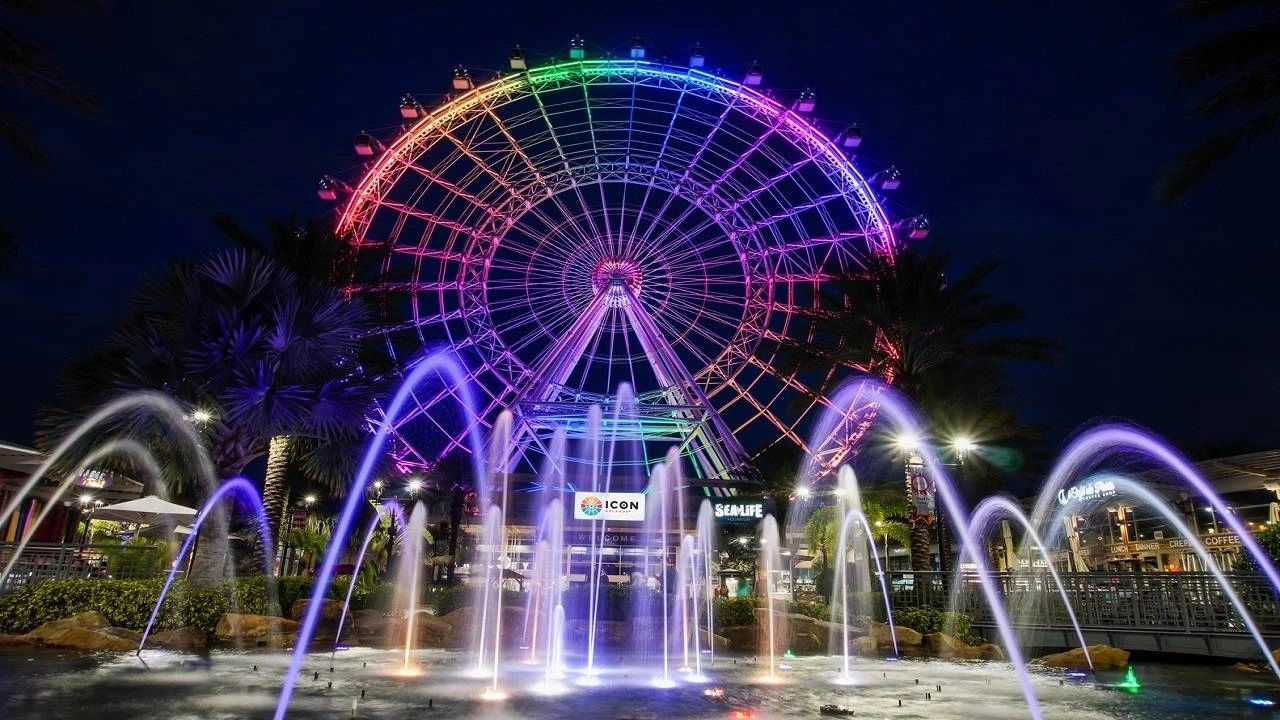 a large colorful Ferris wheel at night with a fountain in front of it