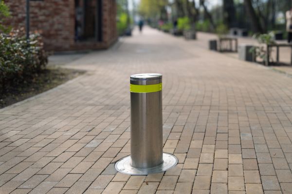 A metallic bollard with a yellow reflective strip on a brick pathway.