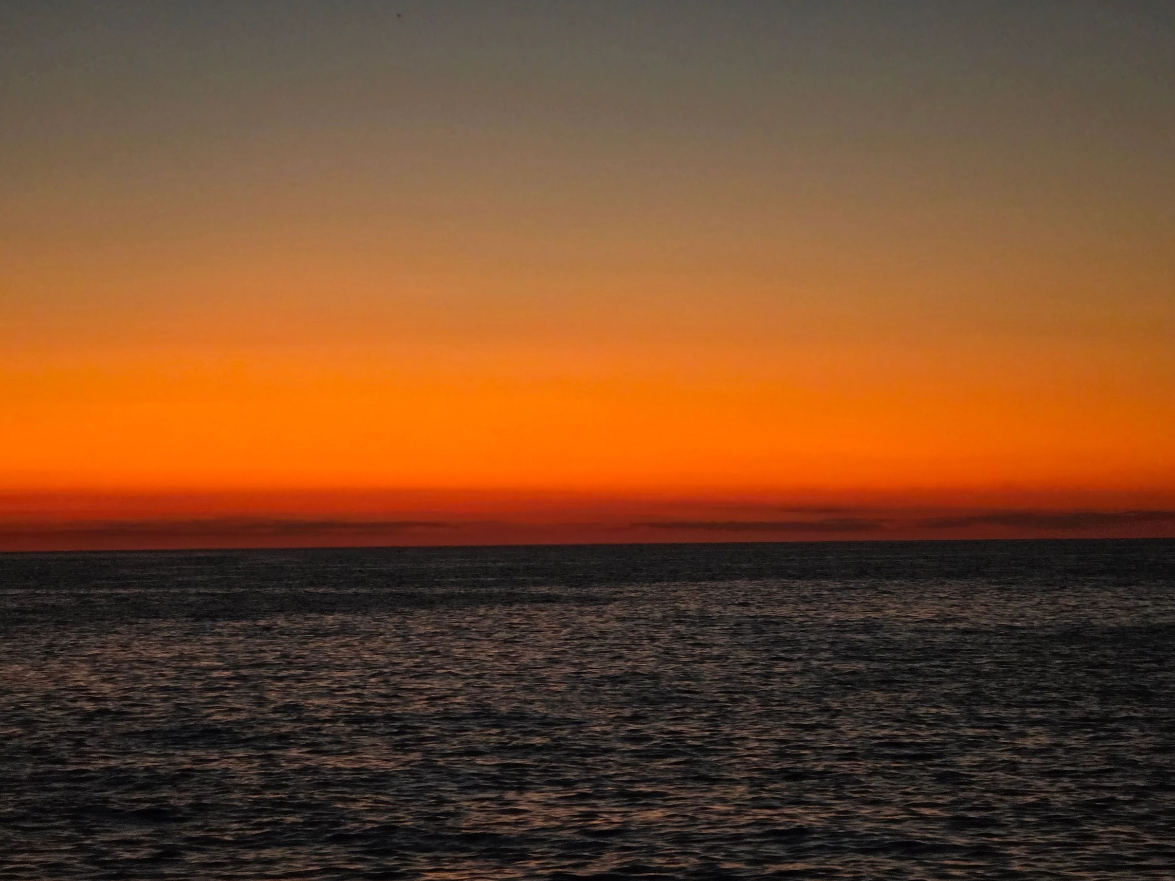 Ocean sunset with vibrant orange and dark horizon.