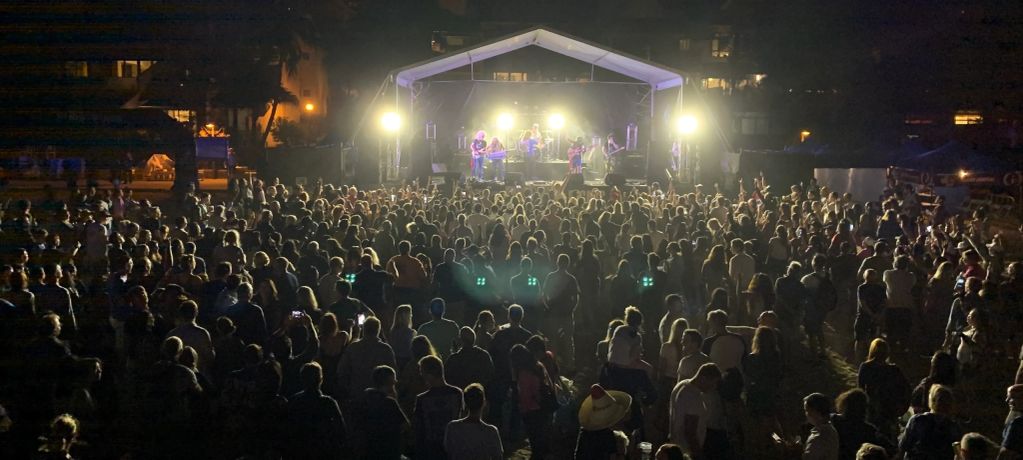 Crowd enjoying a nighttime outdoor concert with bright stage lights.