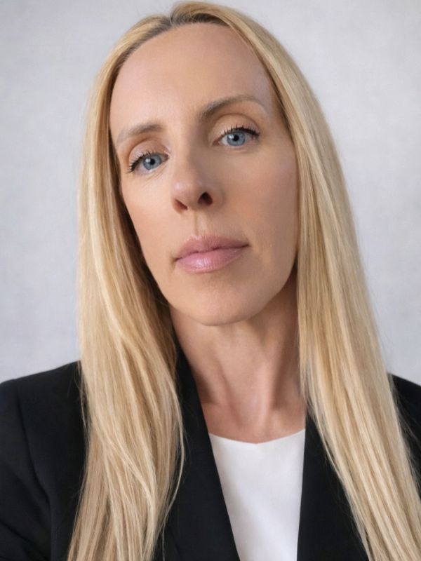 Close-up portrait of a blonde woman with blue eyes in a black blazer.