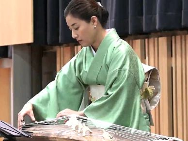 Woman in green kimono playing a traditional string instrument.