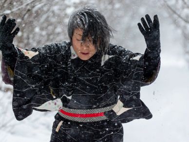 Person in traditional clothing enjoying falling snow outdoors.