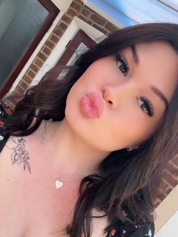 Young woman with dark hair puckering lips for a selfie outdoors.