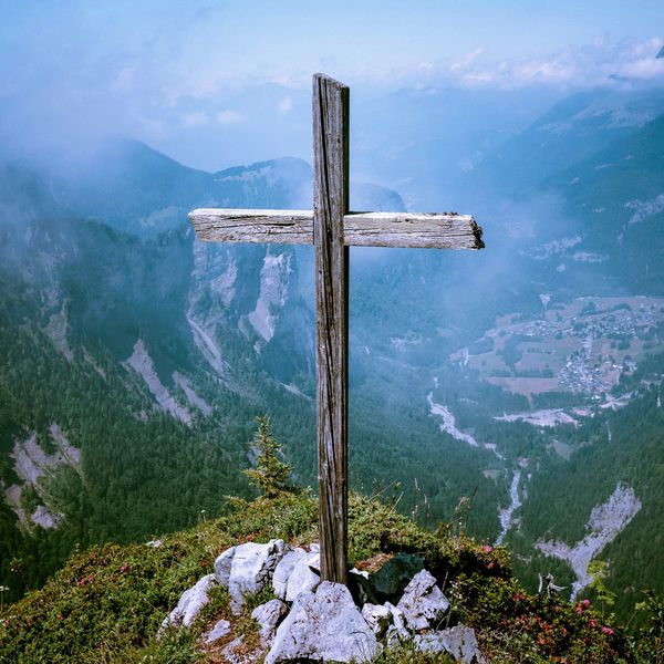 A weathered wooden cross on a mountain peak overlooking a misty valley.