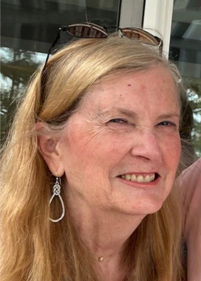 Smiling woman with long blonde hair and sunglasses on her head.