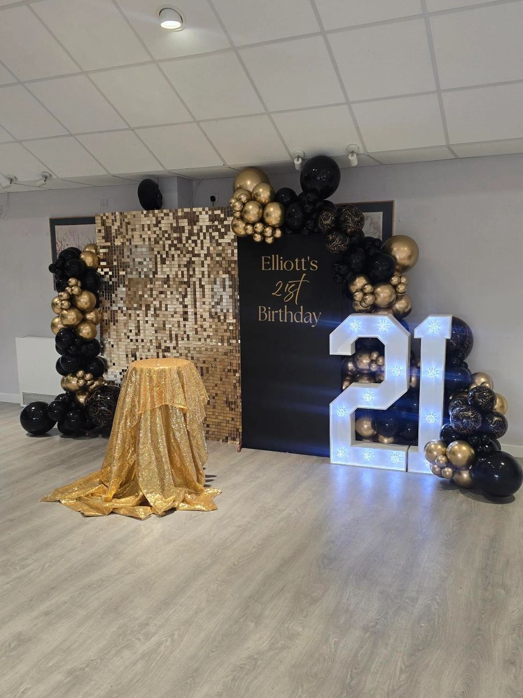 Gold and black 21st birthday party setup with balloons and illuminated numbers.
